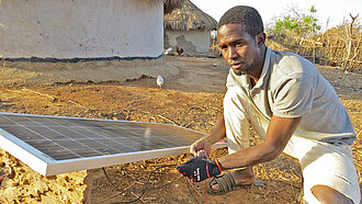 Ein junger Mann kniet vor einem Solarpanel