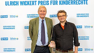 Ulrich Wickert steht gemeinsam mit Journalist Wolfgang Bauer vor einer Werbewand für den Journalistenpreis