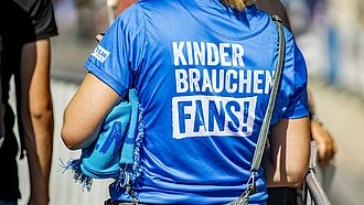 Eine Frau trägt ein T-Shirt der Kampagne "Kinder brauchen Fans!"