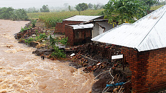 Reißende Wassermassen, daneben zerstörte Häuser