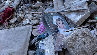 Trümmerteile von Häusern liegen auf dem Boden, darin liegt ein Bild von einem Kind