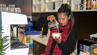 Eine junge Frau gießt geschäumte Milch in eine Kaffeetasse