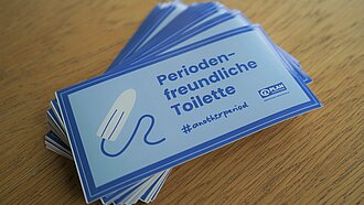 Ein Stapel Sticker mit der Aufschrift Periodenfreundliche Toilette