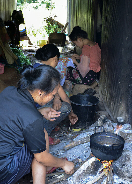 Eine Gruppe Frauen sitzt zwischen Häusern und kocht.