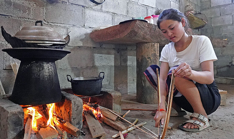 Ein Mädchen kocht an offenem Feuer