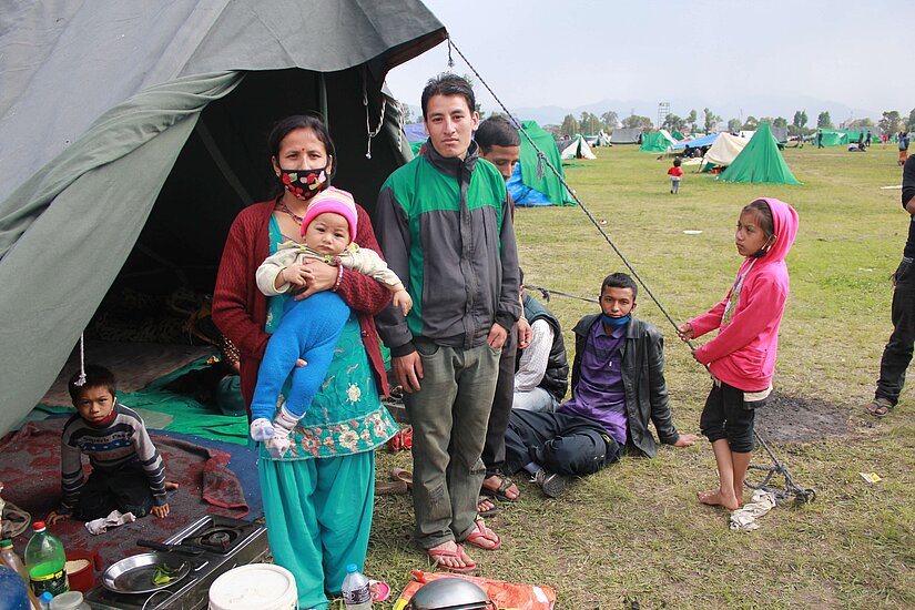 Pramila mit ihrem Mann und ihrem Sohn auf dem Militärgelände in Kathmandu. Das Gebiet dient zurzeit als Zuflucht für Hunderte von obdachlosen gewordenen Menschen. © Plan International