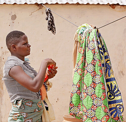 Damipi kümmert sich nach der Schule um die tägliche Hausarbeit Ein Mädchen hängt bunte Tücher auf eine Wäscheleine
