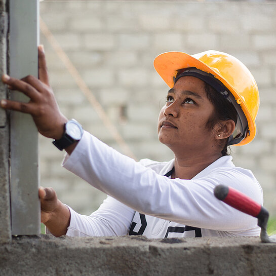 Dilara mit einem gelben Helm begradigt eine Mauer.