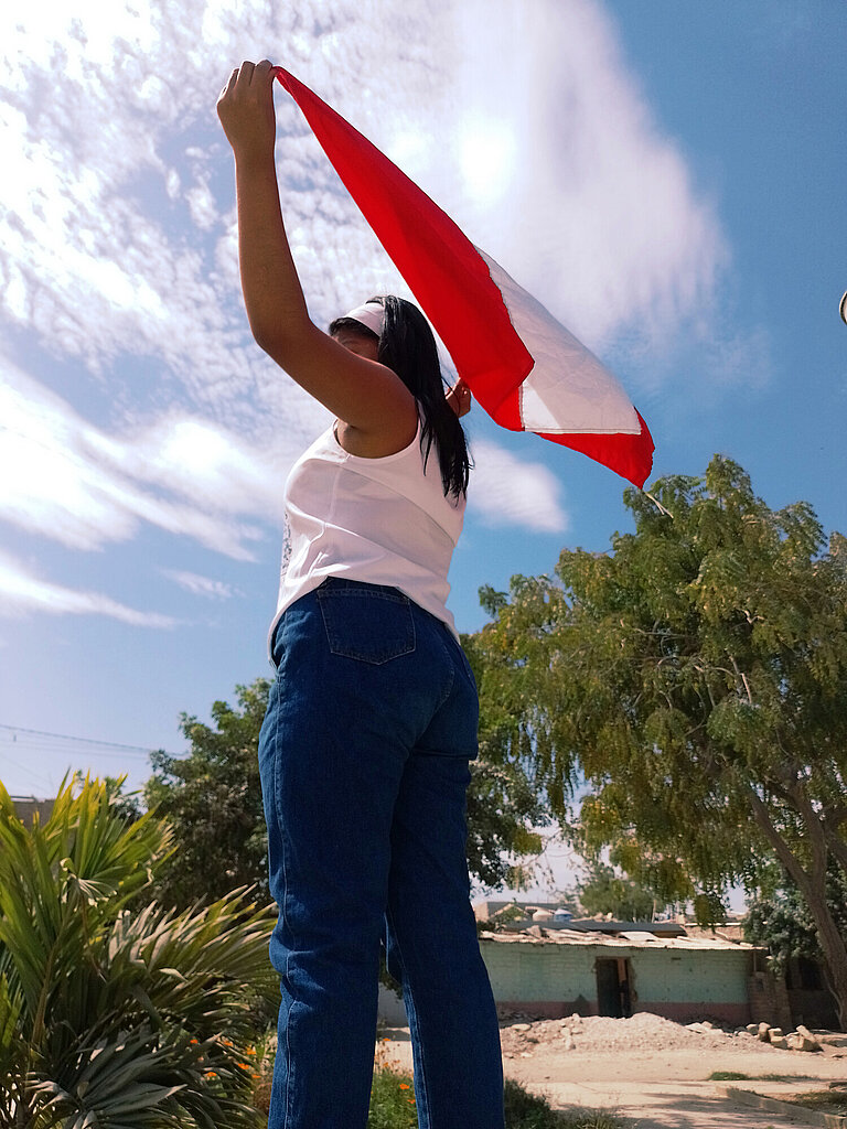 Ein Mädchen von hinten unten fotografiert, das draußen steht und eine peruanische Flagge nach oben hält