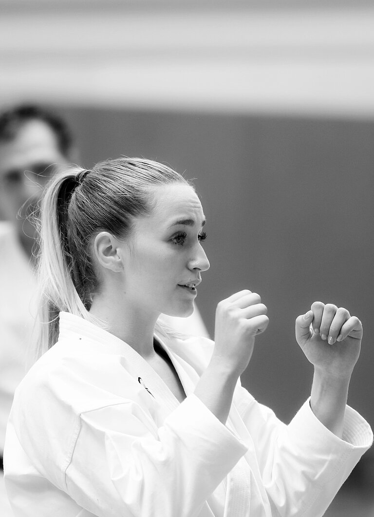 Eine Frau im Karate-Anzug hält die Arme kampfbereit vors Gesicht