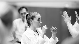 Eine Frau im Karate-Anzug hält die Arme kampfbereit vors Gesicht