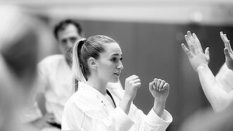 Eine Frau im Karate-Anzug hält die Arme kampfbereit vors Gesicht