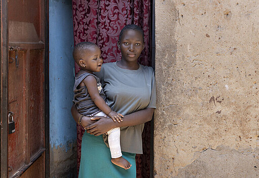 Faith mit ihrer Tochter im Arm in der Haustür stehend