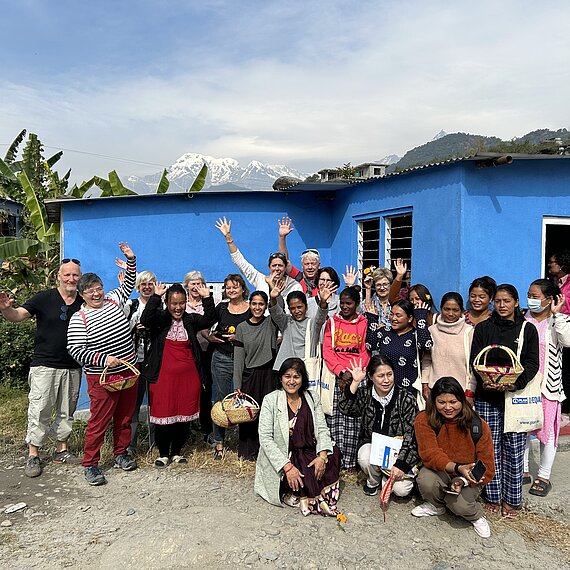 Gruppenfoto einer Projektreise in Nepal, Unterstützende und Projektteilnehmende mit einem blauen Gebäude und dem Himalaya im Hintergrund.