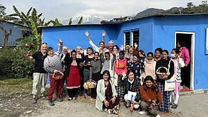 Gruppenfoto einer Projektreise in Nepal, Unterstützende und Projektteilnehmende mit einem blauen Gebäude und dem Himalaya im Hintergrund.