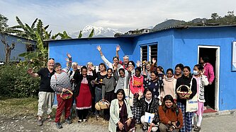 Gruppenfoto einer Projektreise in Nepal, Unterstützende und Projektteilnehmende mit einem blauen Gebäude und dem Himalaya im Hintergrund.