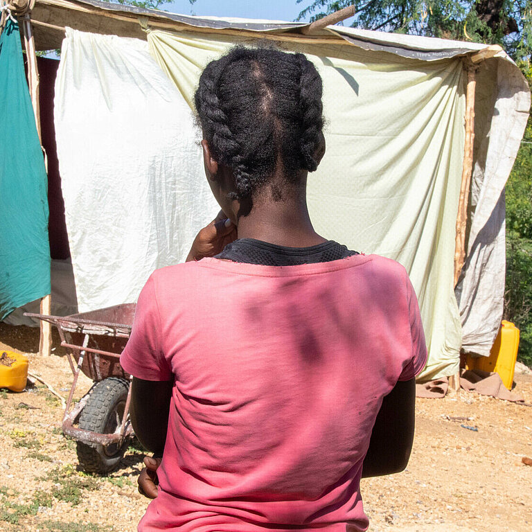 Eine junge Frau steht auf einem trockenen Hügel vor einem provisorisch zusammengebauten Zelt