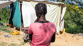 Eine junge Frau steht auf einem trockenen Hügel vor einem provisorisch zusammengebauten Zelt