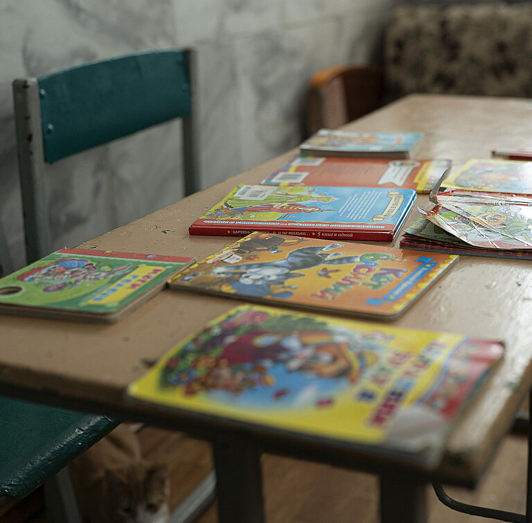 Auf einem Tisch liegen Kinderbücher. Um den Tisch herum stehen kleine Stühle.