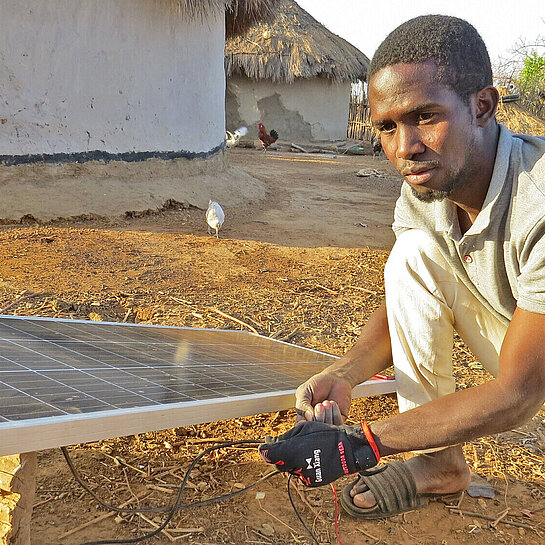 Ein junger Mann kniet vor einem Solarpanel