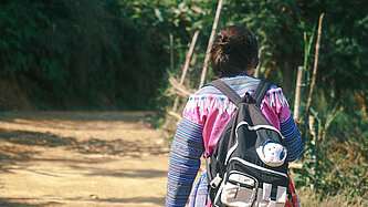 Mädchen mit Rucksack geht einen Weg entlang, Foto von hinten