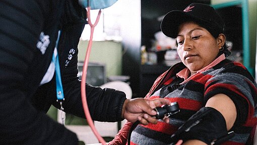 Gesundheitsuntersuchungen für Mütter in Ecuador Eine Frau Sitzt auf einem Stuhl und bekommt ihren Blutdruck gemessen.