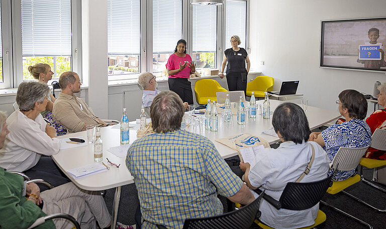 Mehrere Personen sitzen in einem Konferenzraum und hören einer Referentin zu