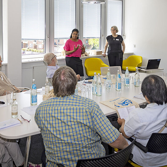 Mehrere Personen sitzen in einem Konferenzraum und hören einer Referentin zu