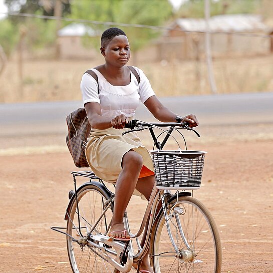 Damipi fährt jeden Tag mit dem Fahrrad zur Schule Ein Mädchen in Schuluniform sitzt mit einem Rucksack auf dem Rücken Fahrrad.
