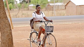 Ein Mädchen in Schuluniform sitzt mit einem Rucksack auf dem Rücken Fahrrad.