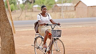 Damipi fährt jeden Tag mit dem Fahrrad zur Schule Ein Mädchen in Schuluniform sitzt mit einem Rucksack auf dem Rücken Fahrrad.