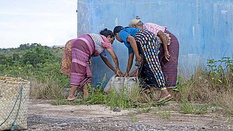 Drei Frauen in bunter Kleidung beugen sich zu einem Brunnen
