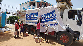Ein LKW mit dem Logo von Plan International wird von mehreren Männern mit Hilfsgütern beladen