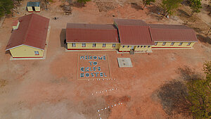 Luftaufnahme der neu errichteten Mädchenwohnheime. Zwei gelbe Gebäude mit roten Dächern, davor aus Steinen gelegt "Welcome to Girls' Hostel"