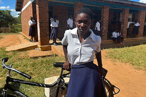 Schülerin steht mit einem Fahrrad vor ihrer Schule in Malawi.