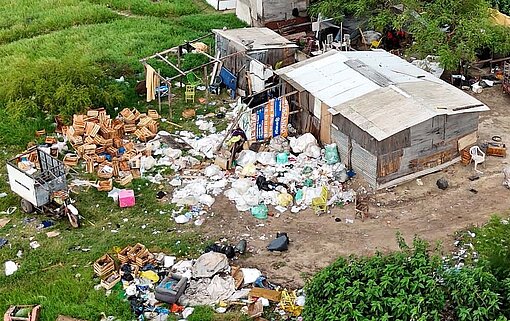 Luftbild einer Wellblechhütte, vor der Berge von Müll liegen