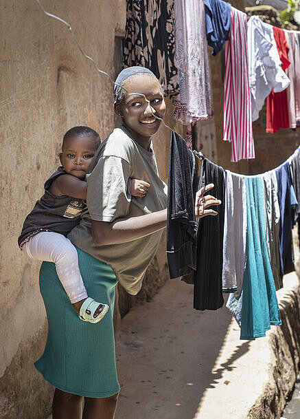 Faith trägt ihre Tochter auf dem Rücken und hängt dabei Wäsche auf