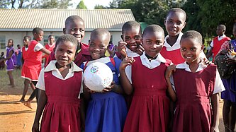 Eine Gruppe von Mädchen aus Malawi steht Freude strahlend zusammen. Sie tragen die Uniformen ihrer Schule und halten einen Fußball in die Kamera.