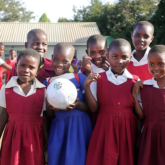 Eine Gruppe von Mädchen aus Malawi steht Freude strahlend zusammen. Sie tragen die Uniformen ihrer Schule und halten einen Fußball in die Kamera.