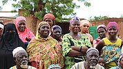 Eine größere Gruppe von Frauen und Männern in bunten, traditionellen Kleidungsstücken steht draußen, einige lächeln.