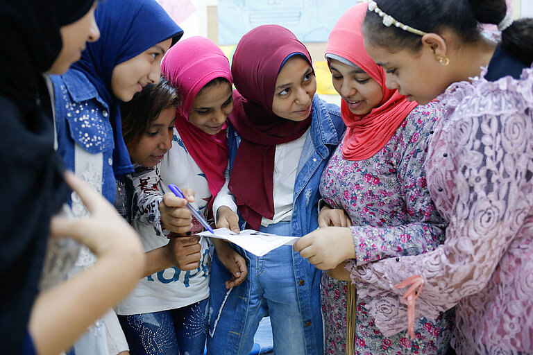 Eine Gruppe Mädchen hat die Köpfe über einem Blatt Papier zusammengesteckt und redet miteinander.