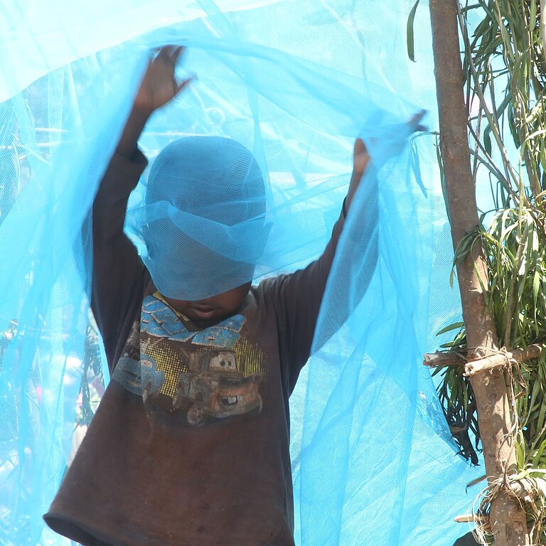 Junge in Ruanda spielt mit Moskitonetz
