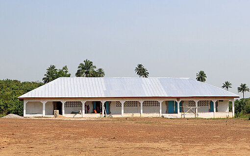 Am Rande eines sandigen Sportplatzes steht ein schneeweiß gestrichenes, flaches Gebäude