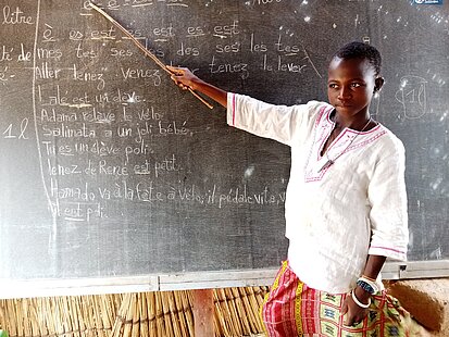Ein Kind zeigt mit einem Zeigestock auf eine Tafel