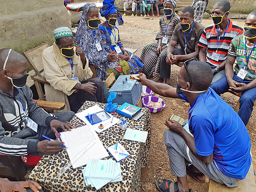 In Guinea sitzen mehrere Personen mit einer Kasse zusammen.