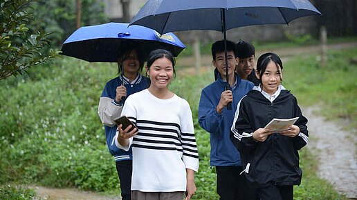 Mehrere Kinder laufen lachend mit Regenschirmen durch den Regen.