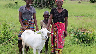 Eine Familie steht mit ihrer Ziege auf einer Wiese.