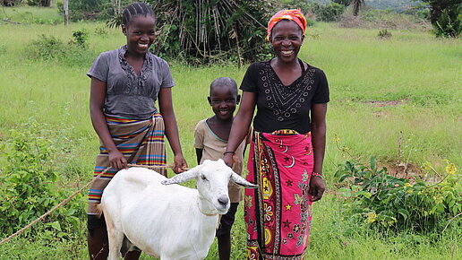 Eine Familie steht mit ihrer Ziege auf einer Wiese.