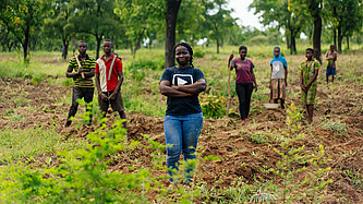 Eine Gruppe junger Menschen steht auf einem Acker und schaut in die Kamera