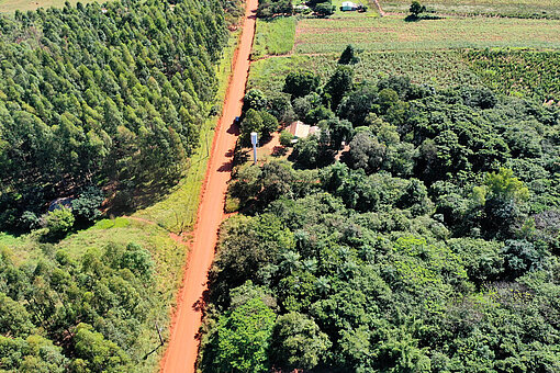 Luftaufnahme einer ländlichen Gemeinde in Paraguay. Eine Straße aus rotem Lehm und grüne Wälder prägen die Landschaft.